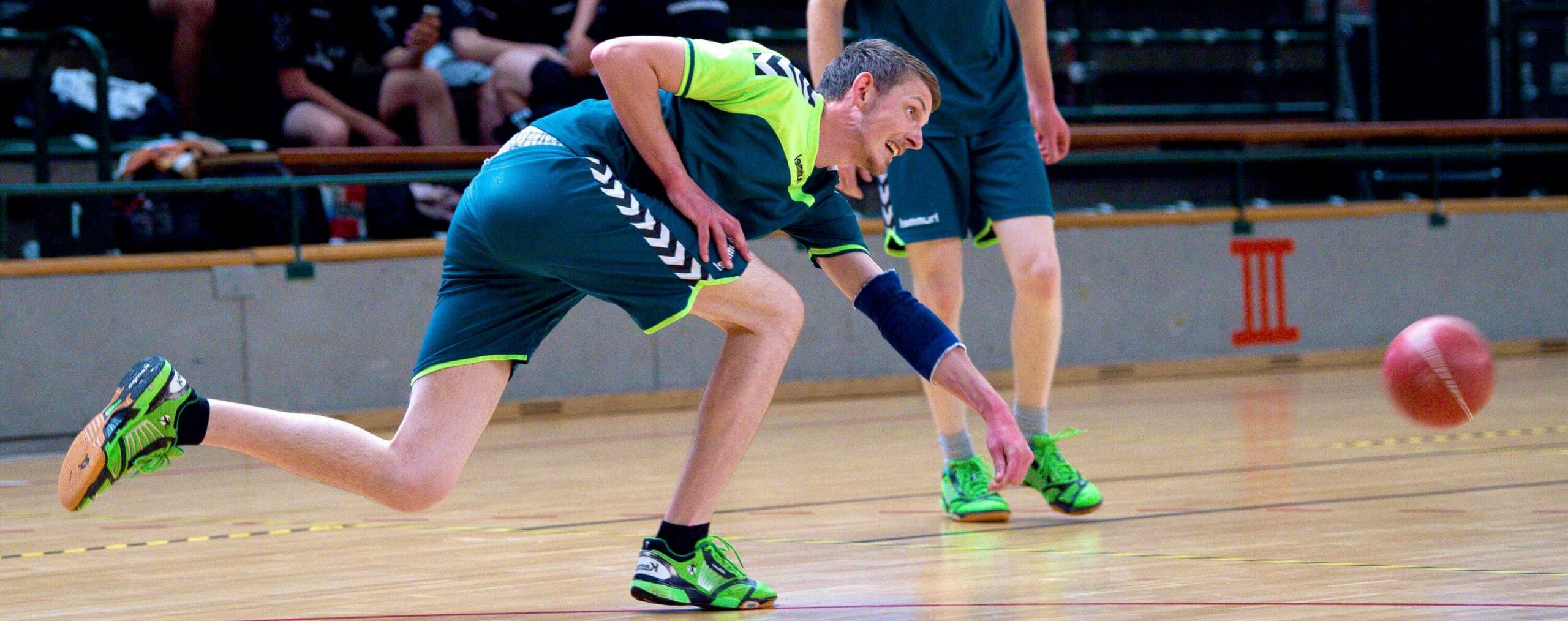 Ein Prellballspieler im grün-blauen Trikot im Spieleinsatz, hechtet nach dem Ball.