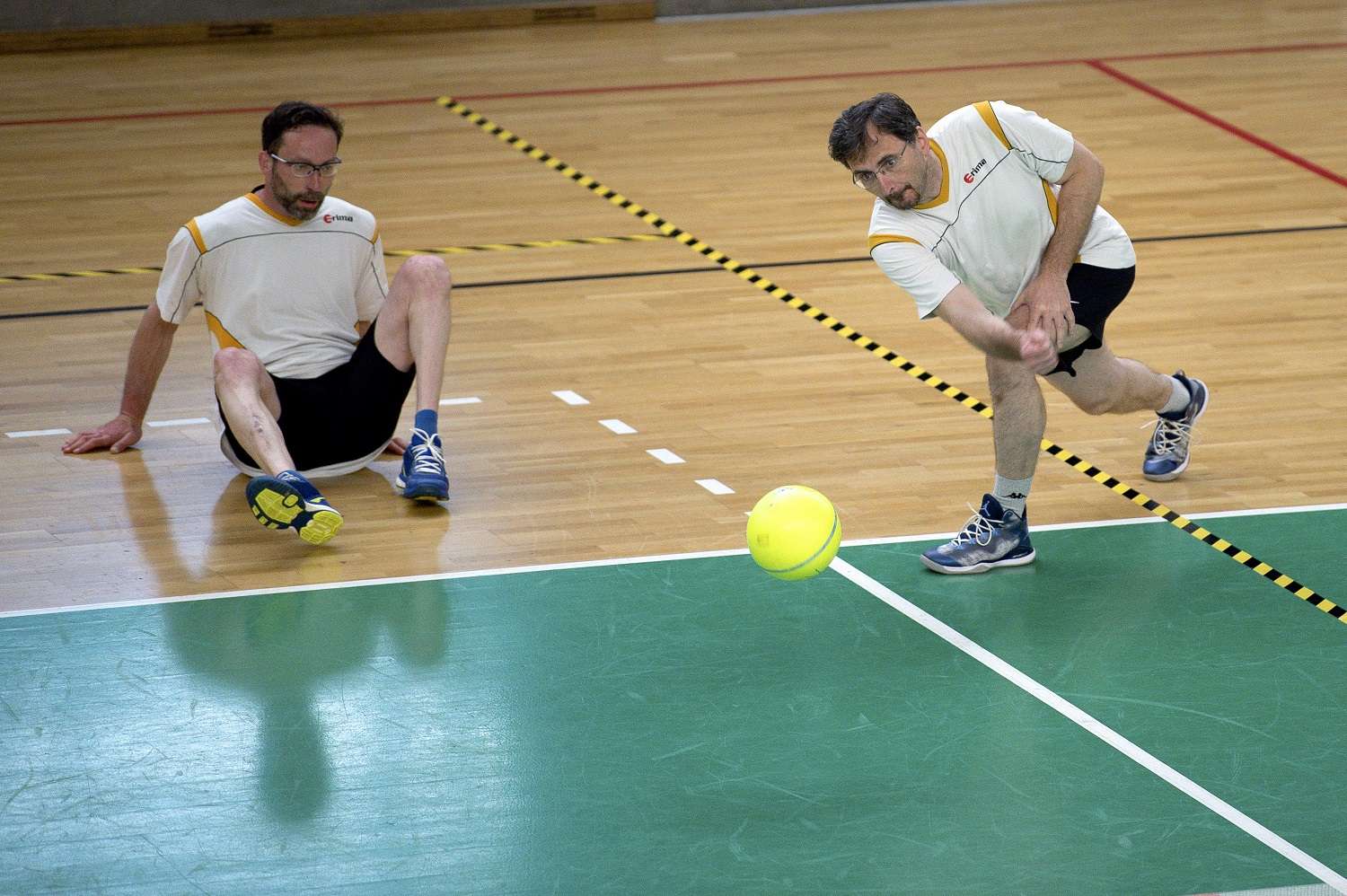 Zwei Prellballspieler in weißen Shirts im Spieleinsatz, der eine hechtet nach dem Ball.