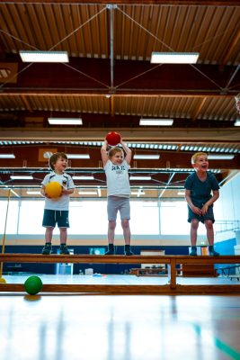 Kinder stehen mit Ball in der Hand auf einer Turnbank