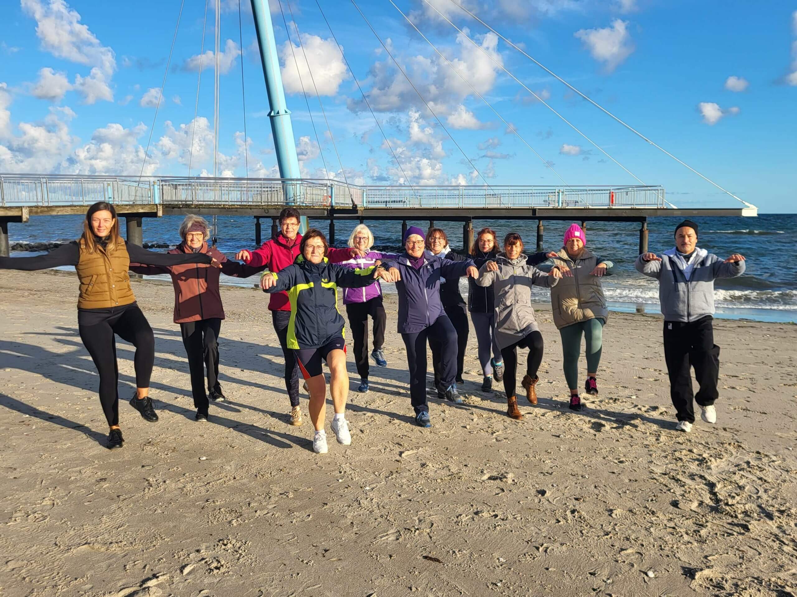 eine Gruppe übt Qigong am Strand - blauer Himmel und Meer