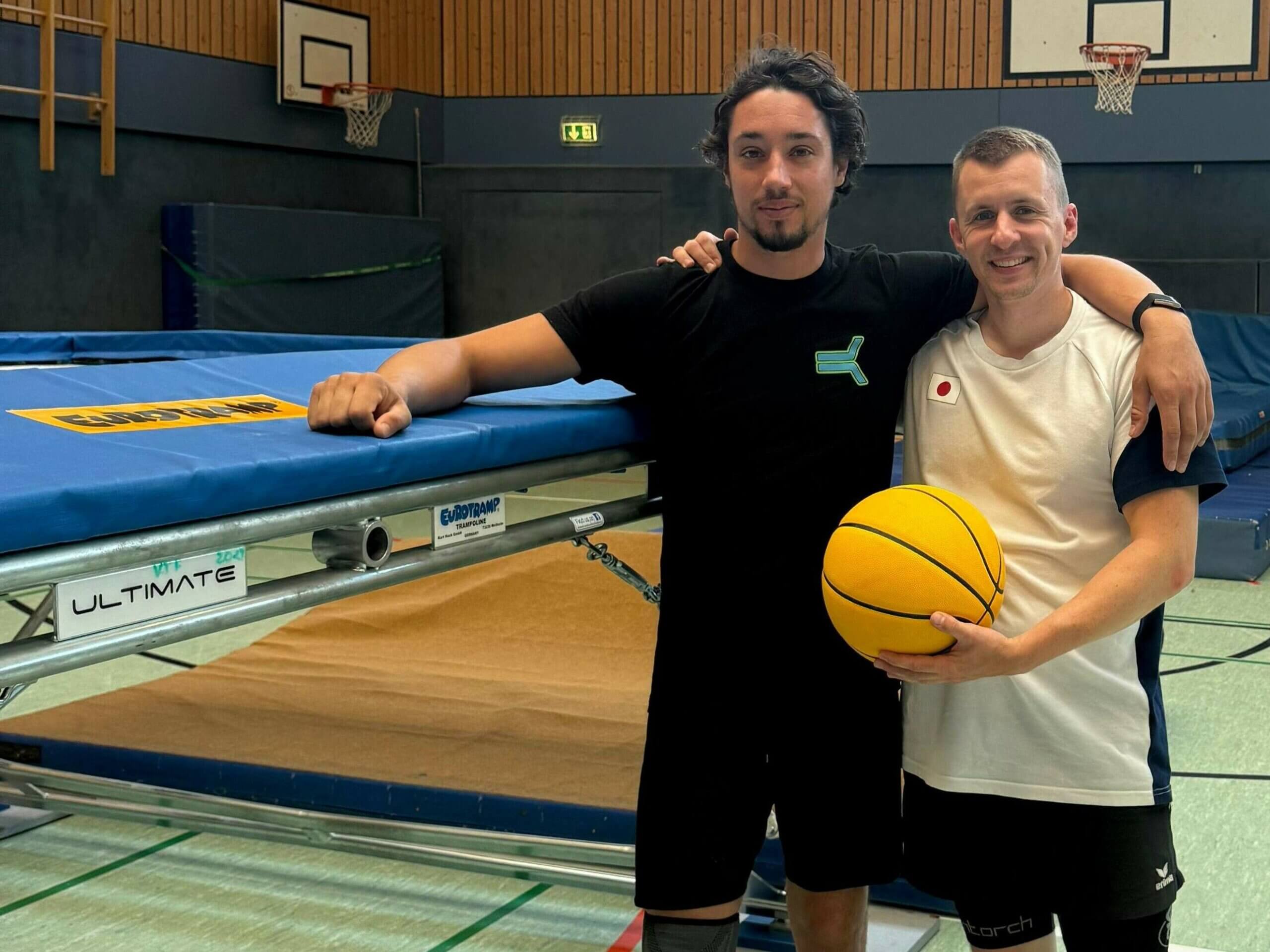 Trampolinspringer Daniel Schmidt und Ninja-Sportler René Casselly stehen mit einem Basketball neben einem Trampolin
