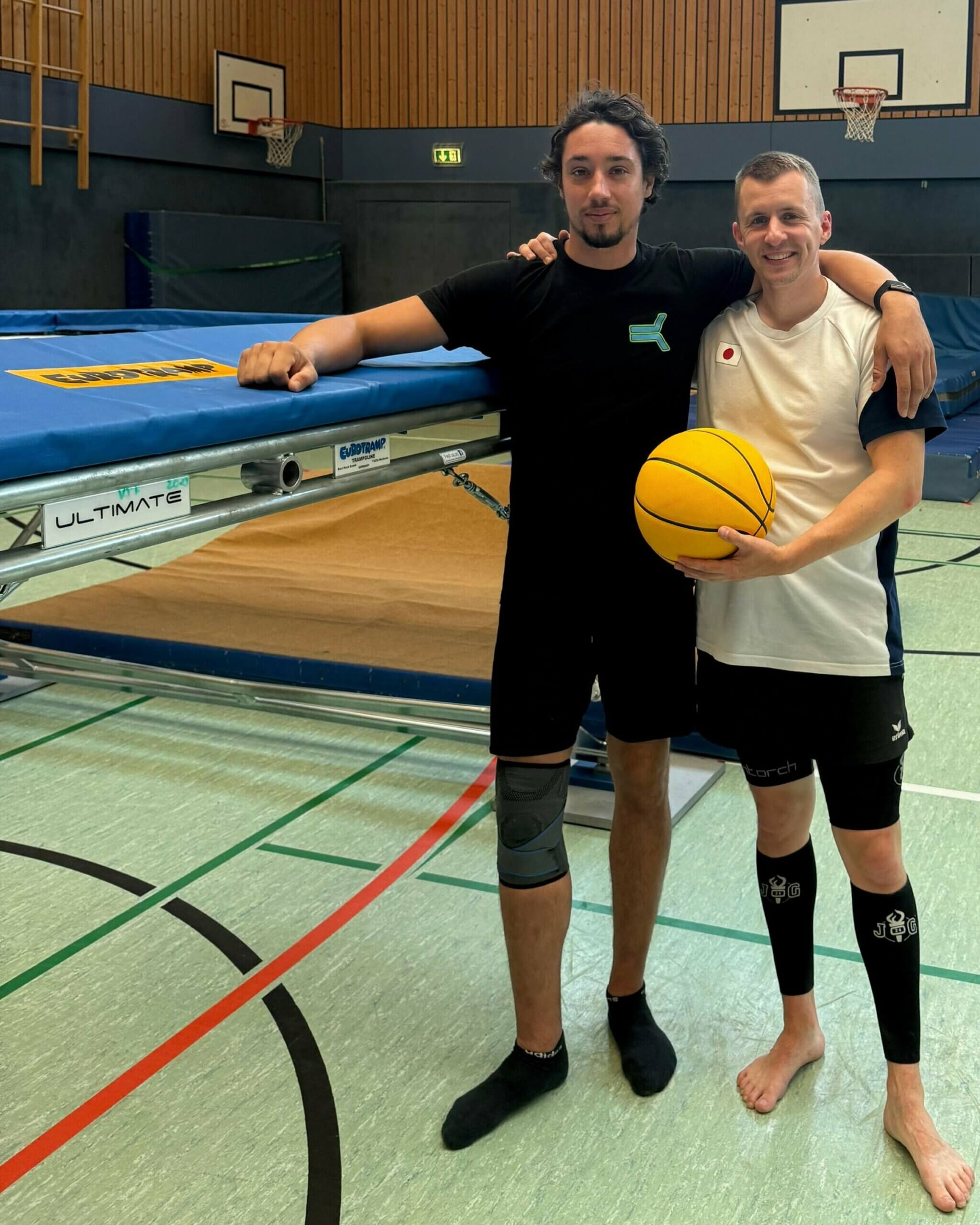 Trampolinspringer Daniel Schmidt und Ninja-Sportler René Casselly stehen mit einem Basketball neben einem Trampolin
