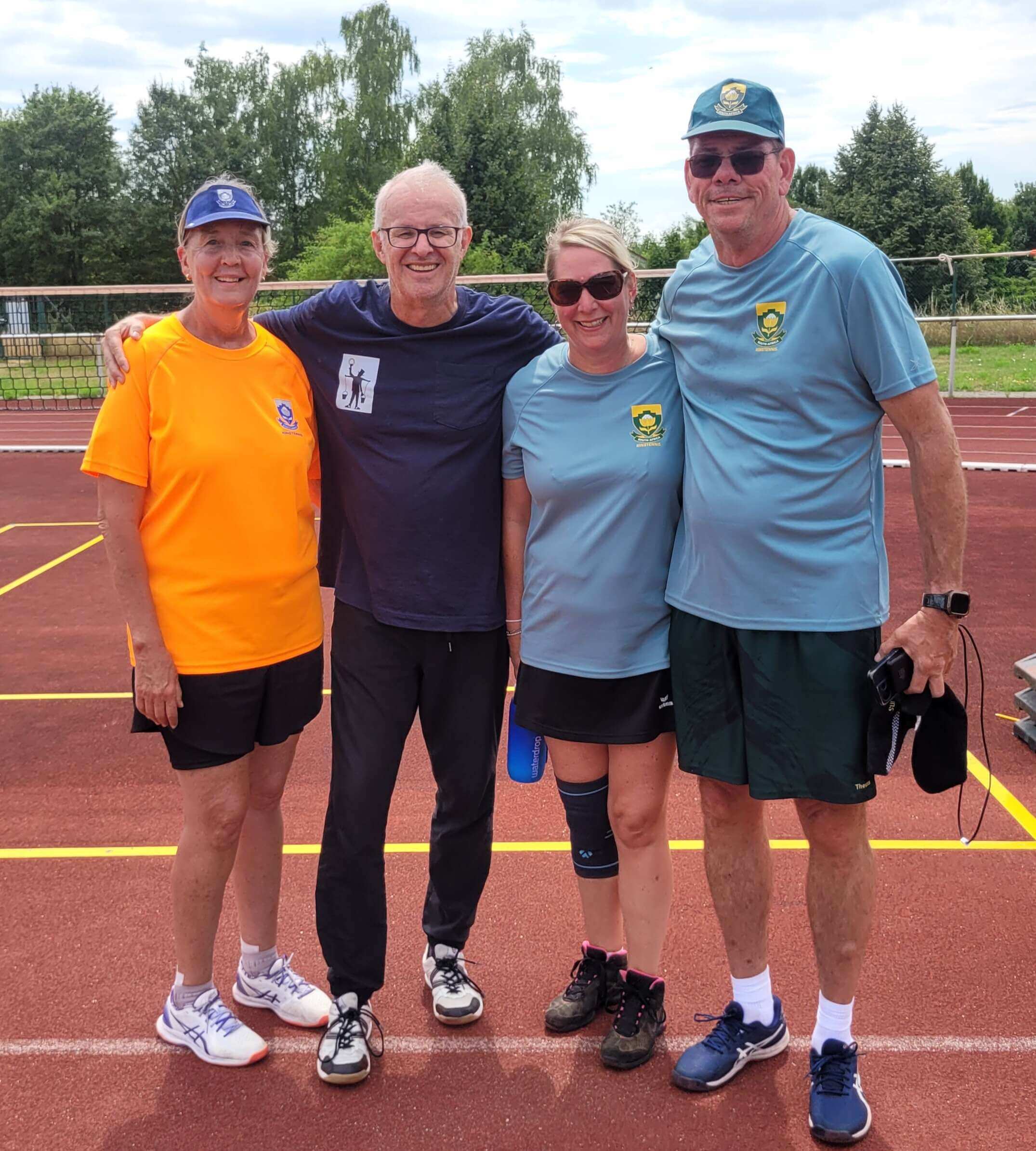 4 Menschen stehen auf einem Ringtennis-Feld und halten sich in den Armen