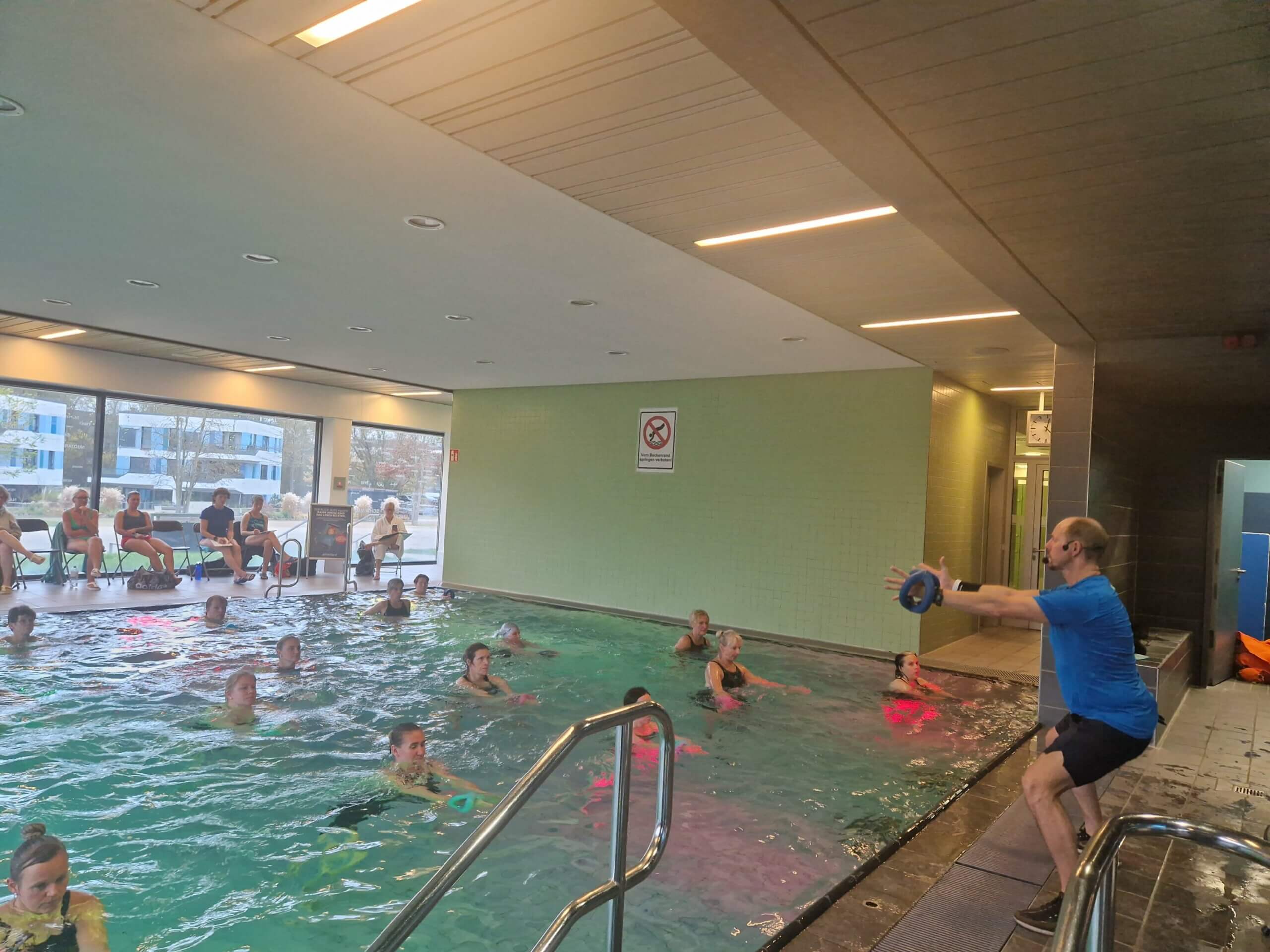 Referent zeigt Aqua-Übung am Beckenrand, Teilnehmende im Wasser