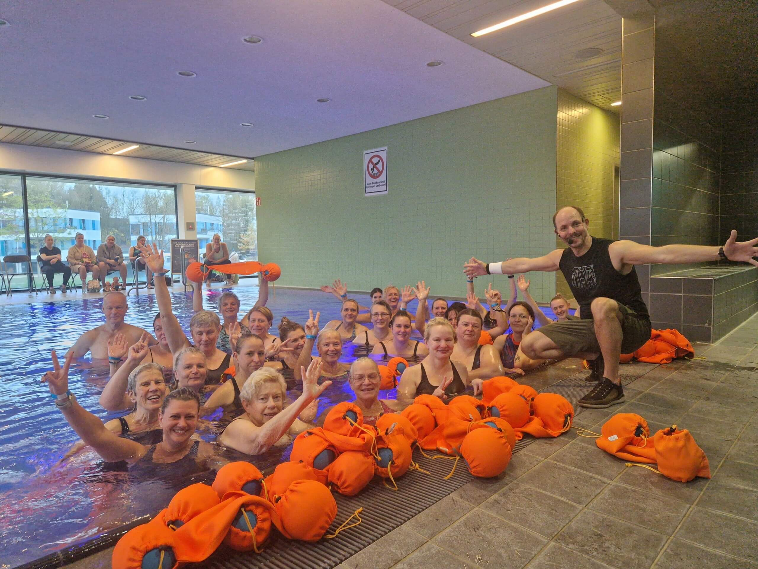 Gruppenfoto vom Aqua-Kongress. Der Referent ist am Beckenrand, die Gruppe im Wasser, vor dem Referenten liegen Aqua-Sportgeräte