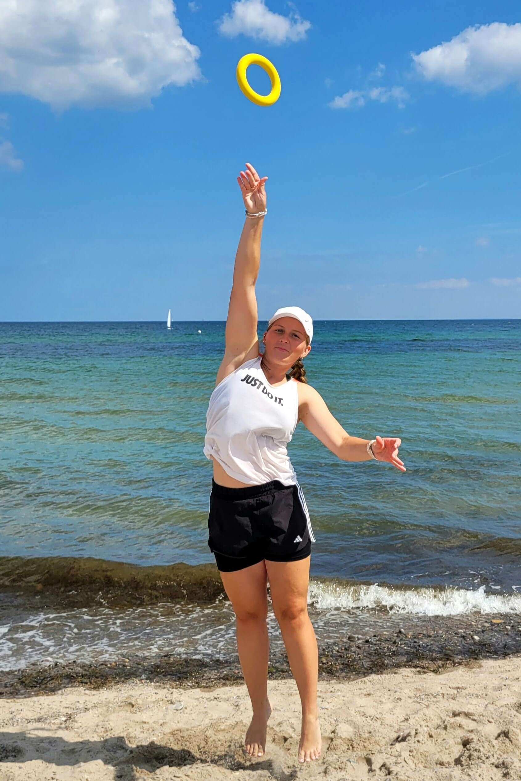 Eine Spielerin wirft den Ring in die Höhe. Im Hintergrund ist die Ostsee und blauer Himmel zu sehen.