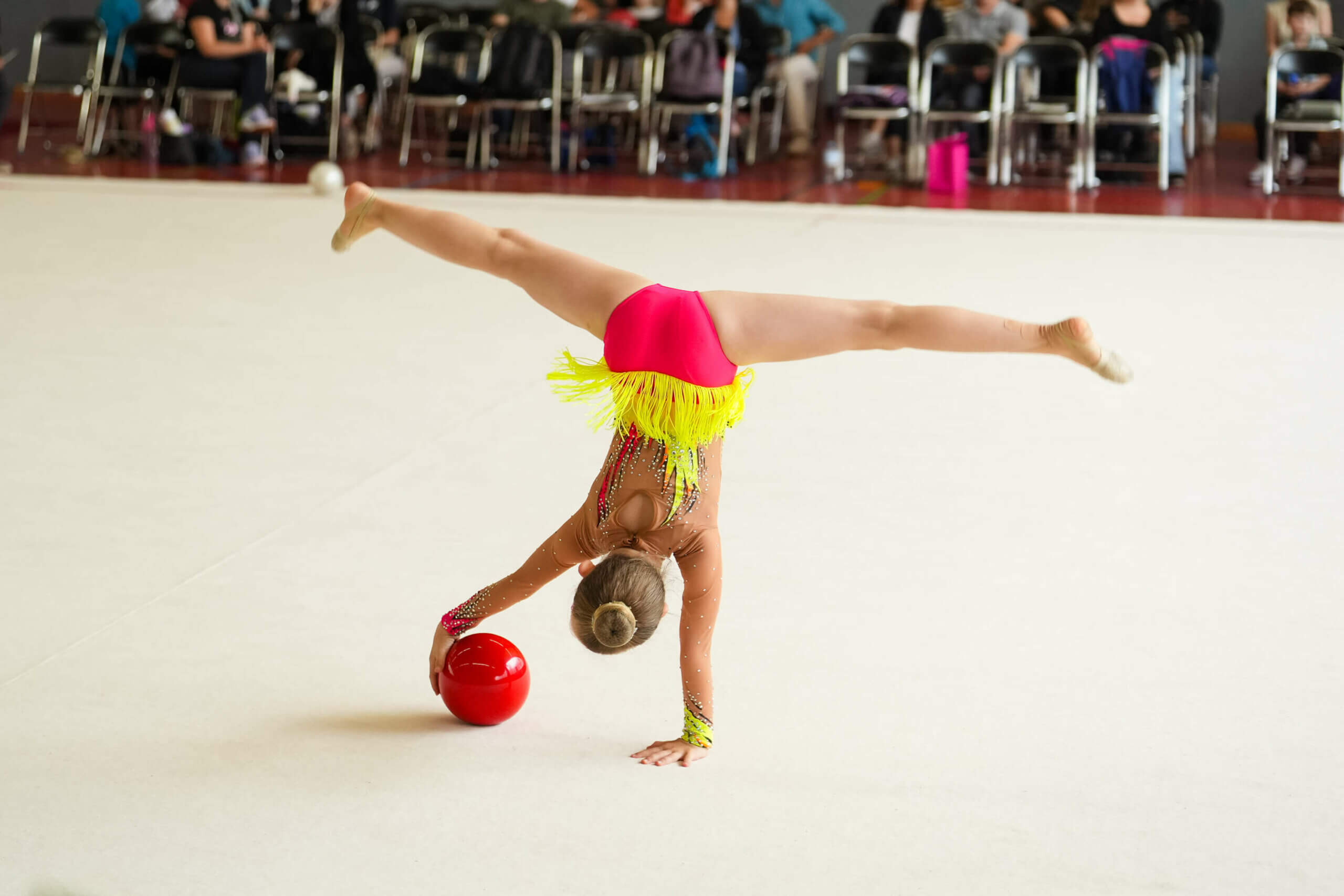 Gymnastin im gegrätschten Handstand mit einem Ball in der rechten Hand