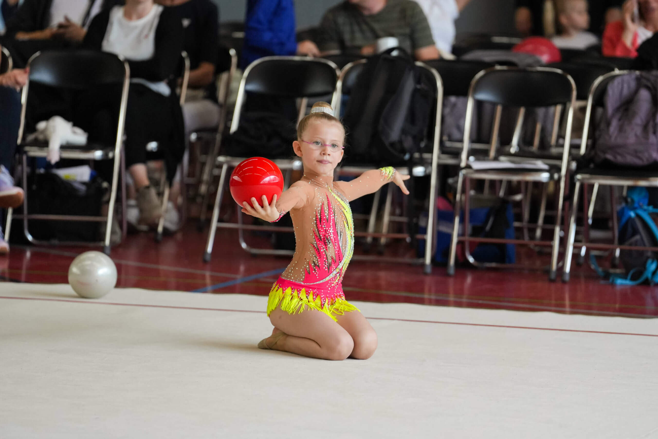 eine Gymnastin kniend mit einem roten Ball in der Hand.