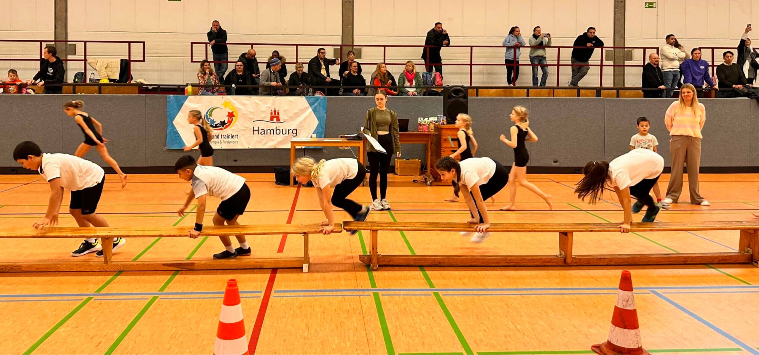 5 Kinder machen hintereinander eine Hockwende an der Bank in einer Turnhalle
