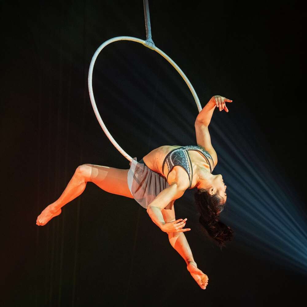 eine Artistin hängt schwebend rücklings in einem großen Ring, dessen Halterungsstange von oben ins Bild hinein ragt