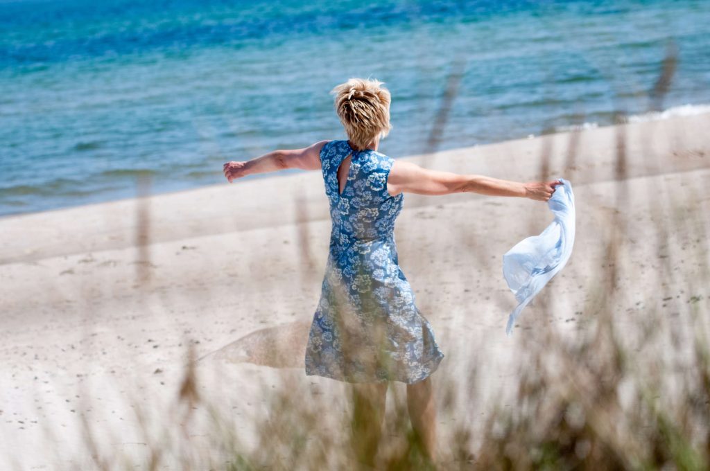 Frau tanzt am Strand von hinten