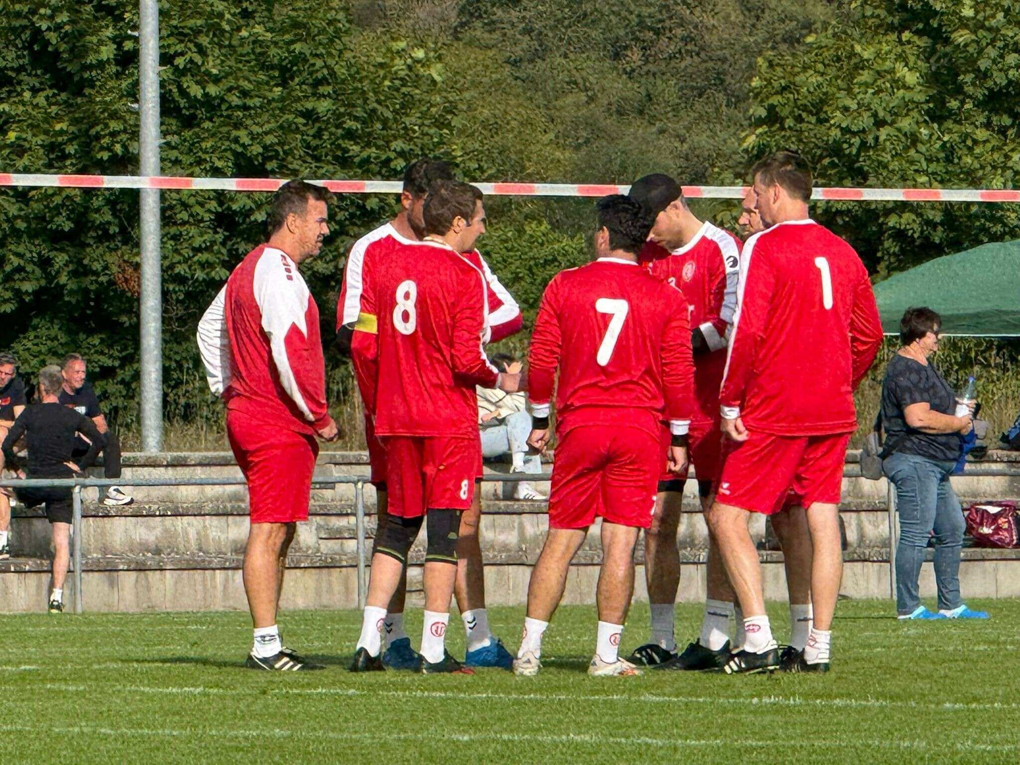Herren-Faustballmannschaft in roten Trikots berät sich im Kreis