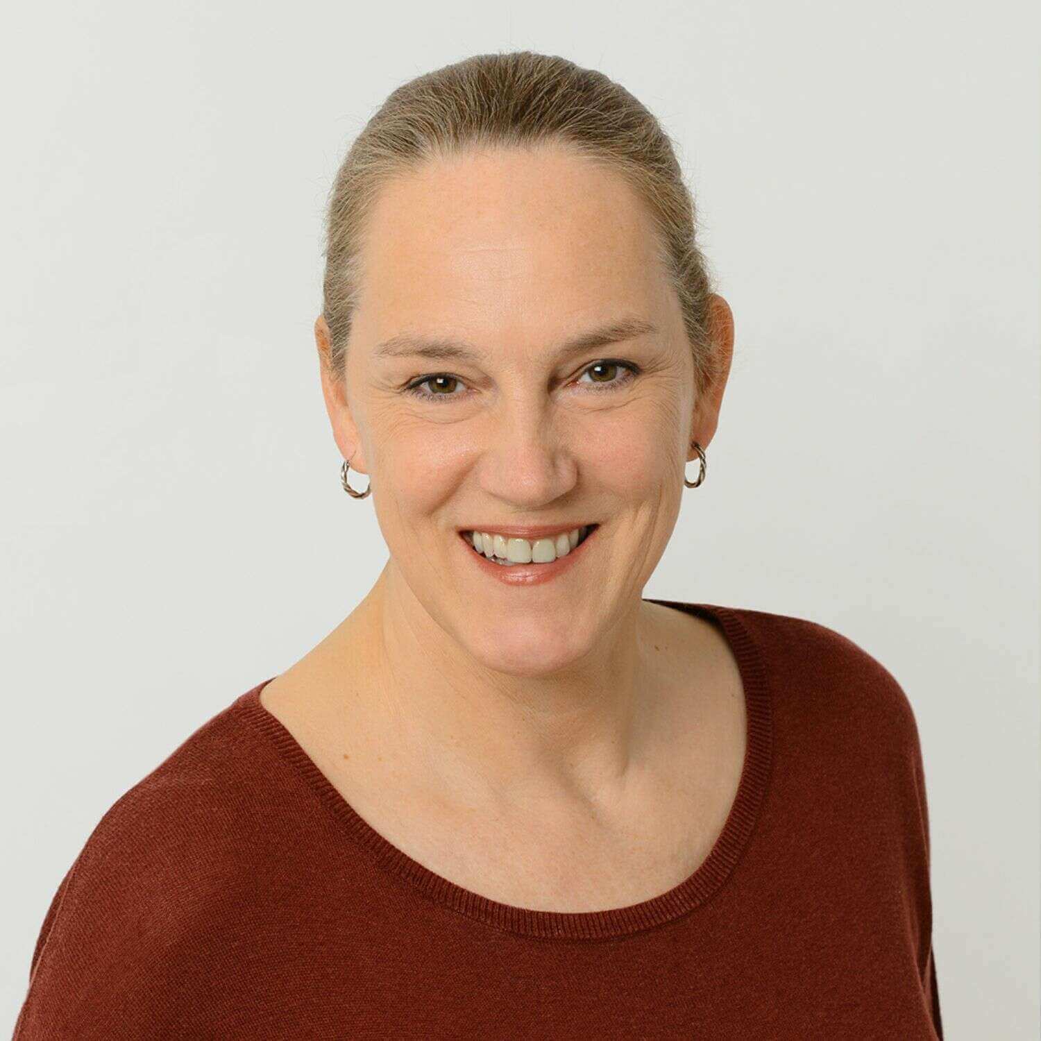 Referentin Caroline Dohmen in dunkelrotem Pullover vor hellgrauem Hintergrund