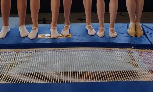 Auf der blauen Randabdeckung eines Doppl-Mini-Trampolins sieht man 5 Fußpaare in Gymnastik-Schuhen stehen.