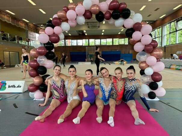 6 Gymnastinnen sitzen im Spagat unter einem Torbogen aus Luftballons