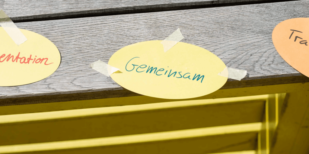 Ein rundes Papier klebt auf einer Holzfläche und dort steht "Gemeinsam" drauf.