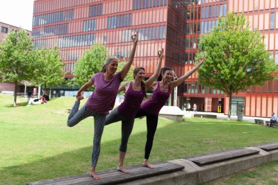Drei Frauen bei einer Yoga-Pose stehend auf einer Bank in vor einer Grünfläche in Hamburg