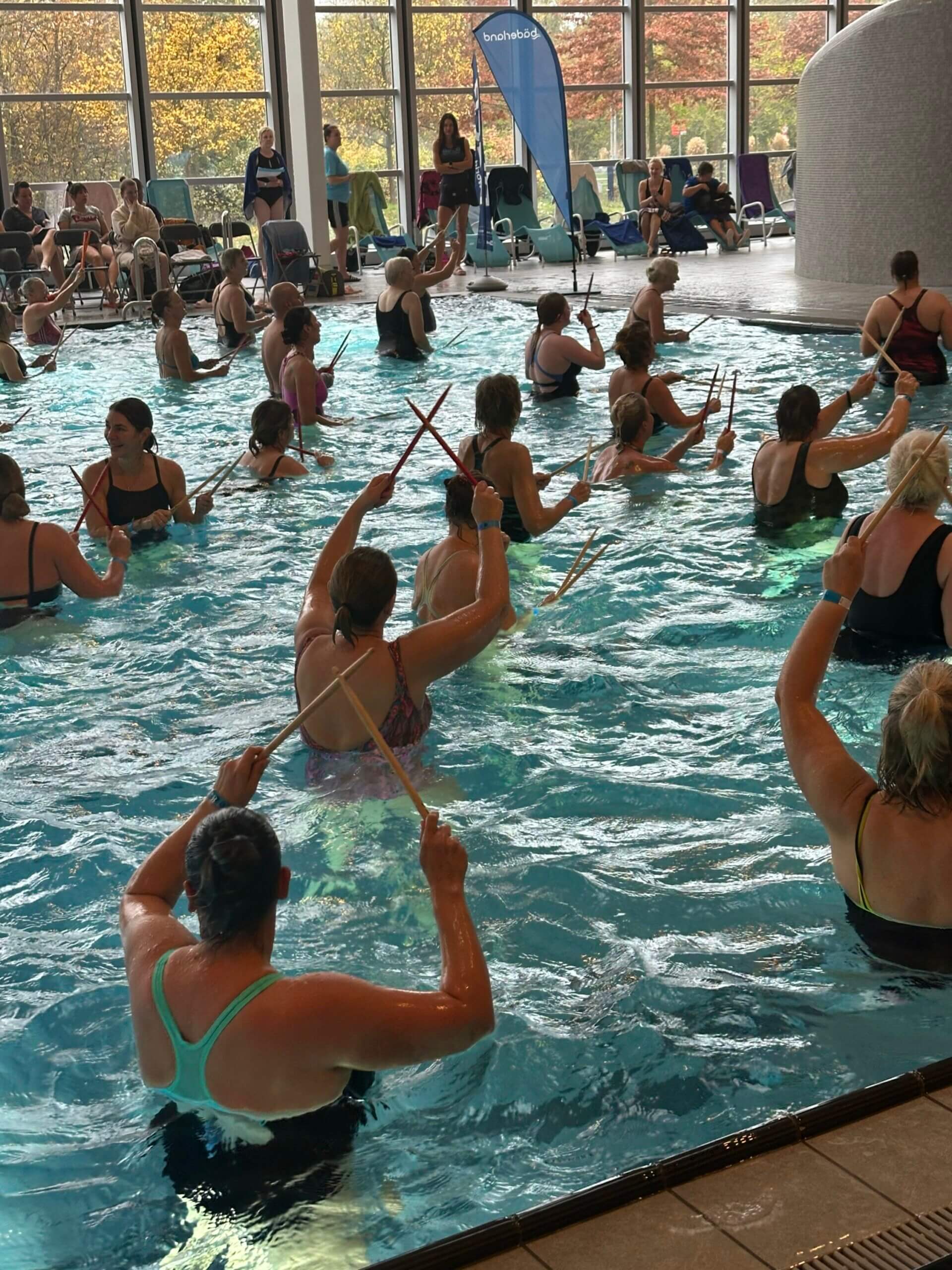 Aqua-Sportler*innen im Wasser halten Drumsticks gekreuzt in die Luft