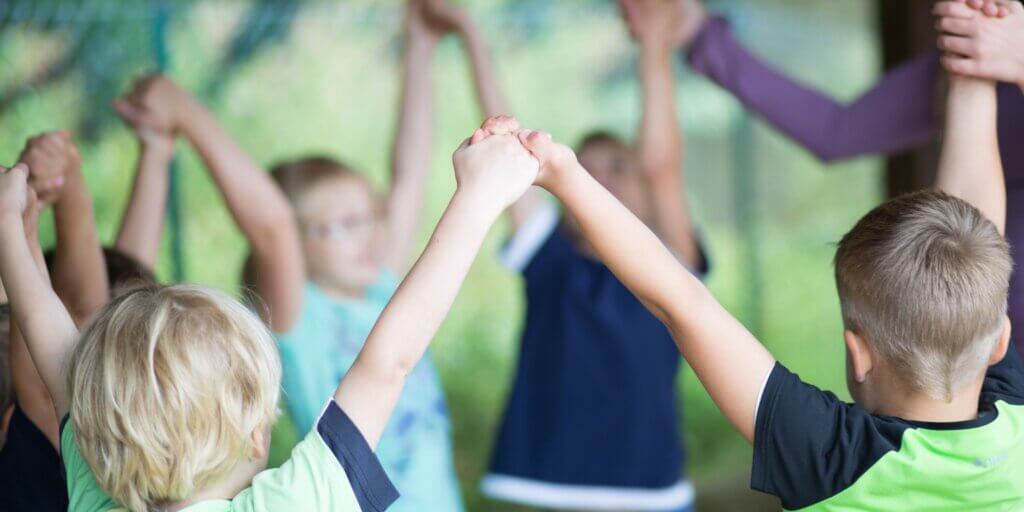 Kinder im Kreis halten sich an den Händen und recken sie in die Höhe
