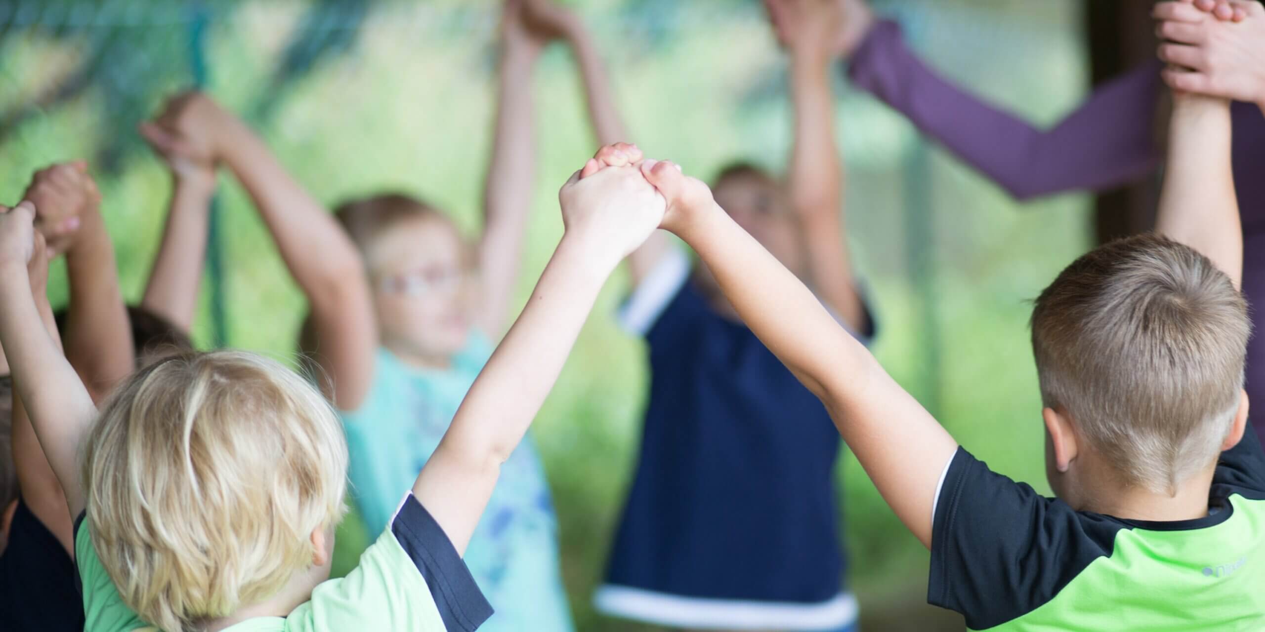 Kinder im Kreis halten sich an den Händen und recken sie in die Höhe