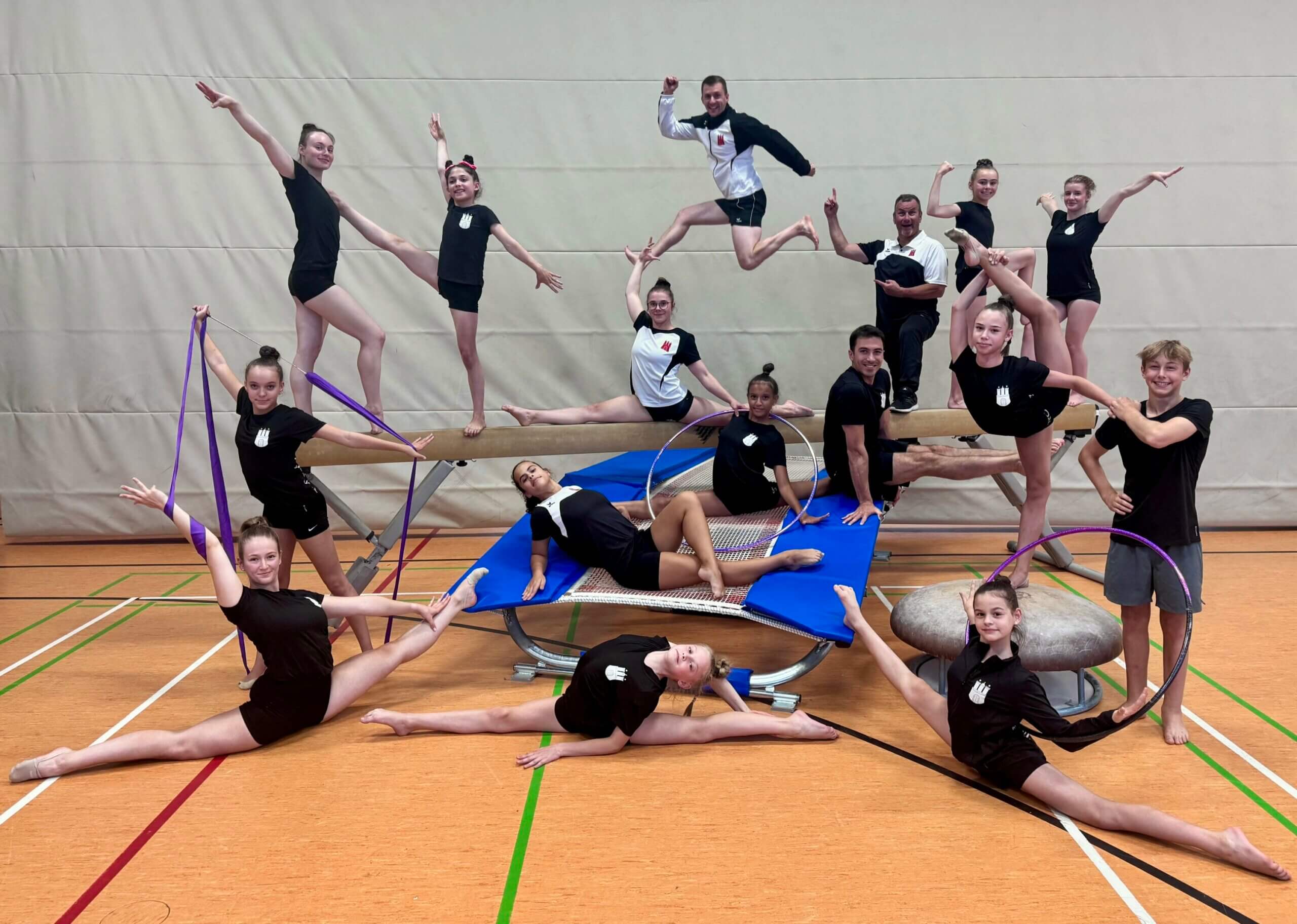 ein Schwebebalken und ein Trampolin und viele Turnerinnen und turner, die Spagat oder eine andere turnerische Pose machen