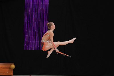 Gymnastin mit Keulen bei einem Sprung mit einem angehockten und einem vorgespreizten Bein