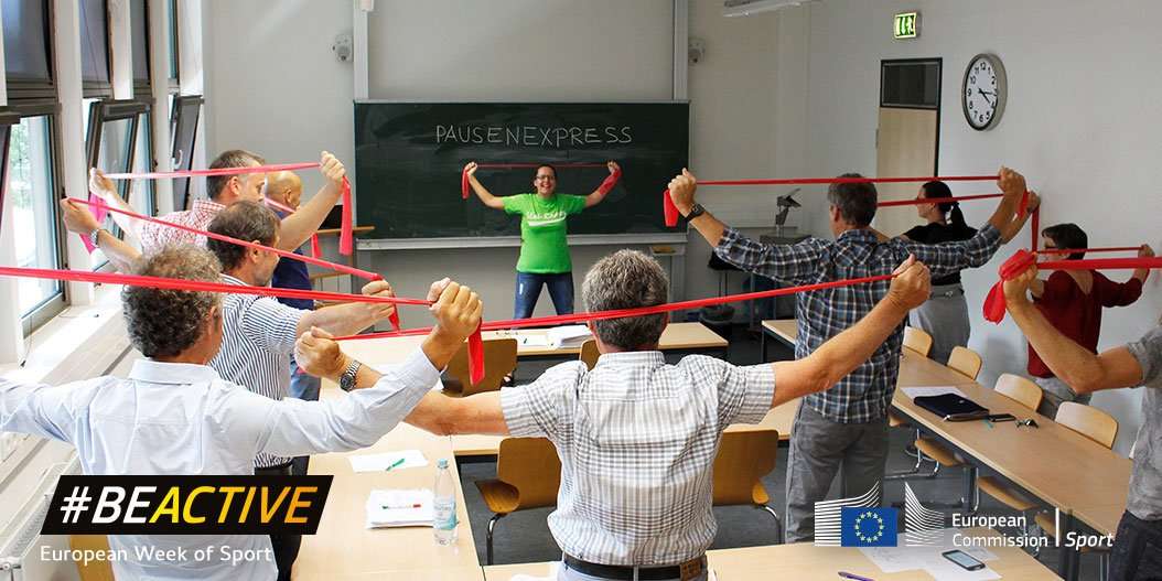 Eine Sportgruppe in einem Raum macht eine Fitnessübung mit dem Theraband.