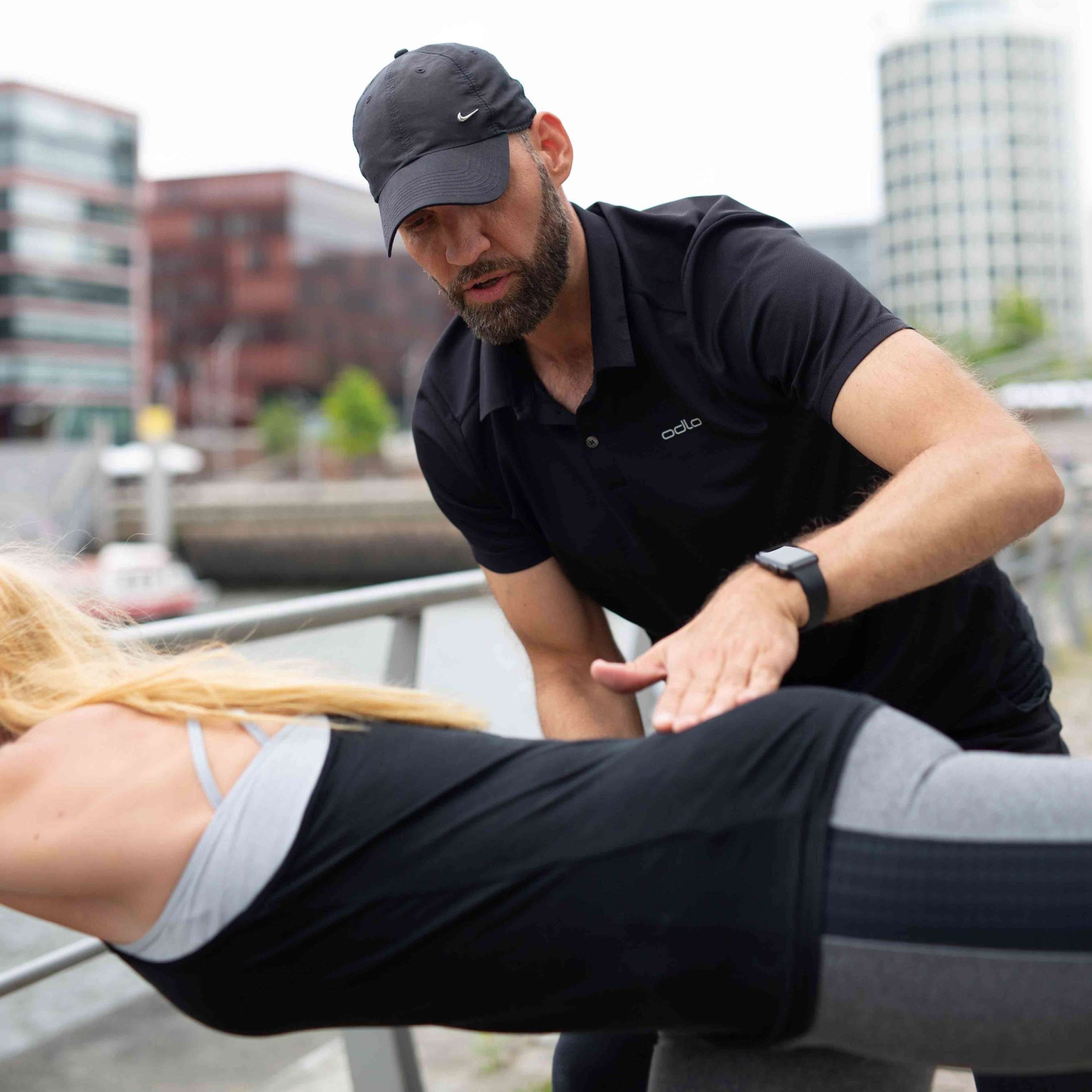 Der Personaltrainer kontrolliert die genaue Ausführung einer Rückenübung, die seine Fitnessportlerin im Liegen ausführt