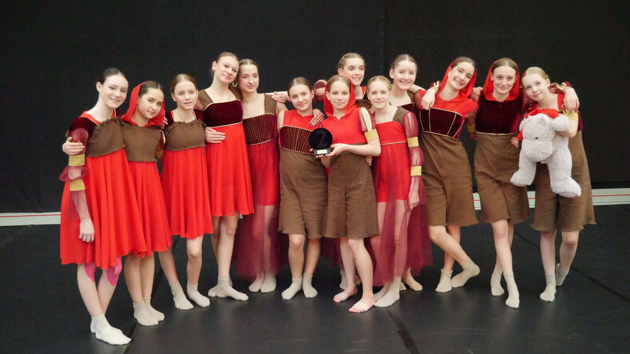 Eine Gruppe von Tänzerinnen, mit knielangen Kleidern in rot und braun gehalten, stehen zusammen zu einem Gruppenbild