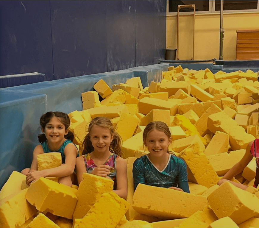 Drei junge Turnerinnen sitzen inmitten von gelben Schaumstoffschnitzeln