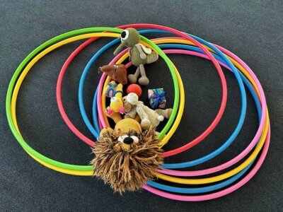 Auf dem Boden liegen bunte Reifen und Kinderspielzeug. In der Mitte ist ein Löwe zu sehen.