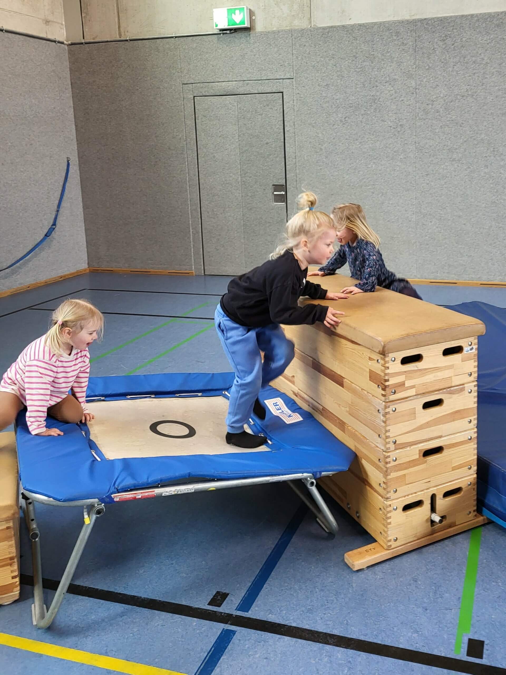 ein kleines Mädchen auf dem kleinen Trampolin versucht auf einen Kasten zu kommen.