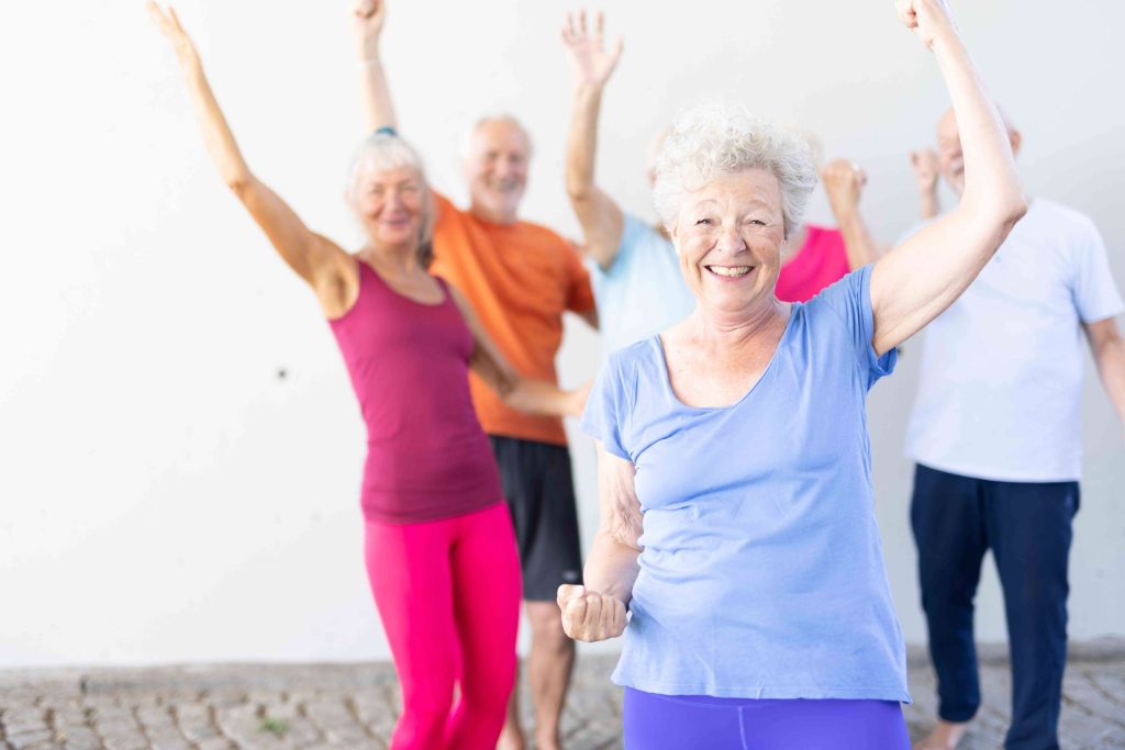 Gruppe älterer Menschen heben beim Fitness mit Freude die Arme abwechselnd