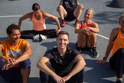 Eine Gruppe von sechs Fitnesssportler*innen sitzen an der Erste, zwei von ihnen schauen in die Kamera