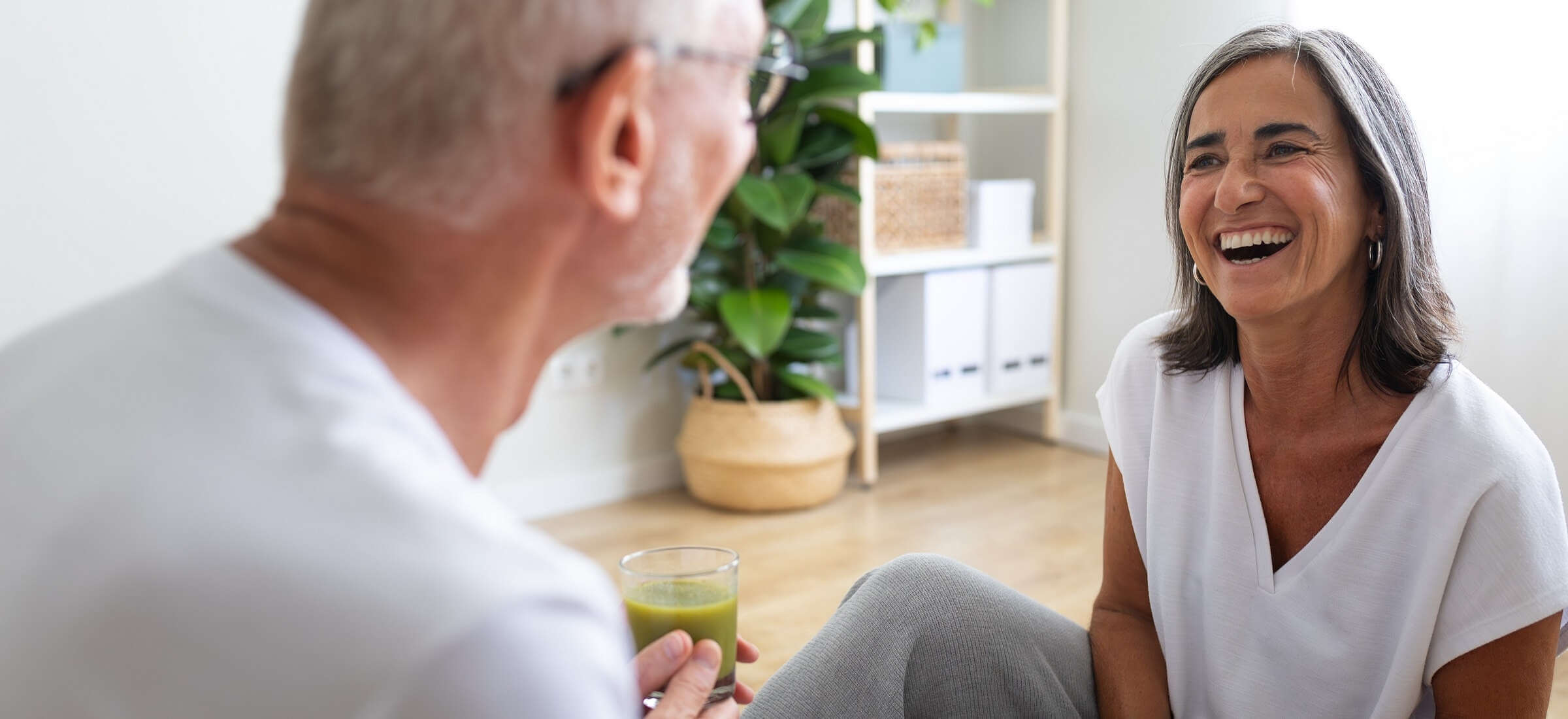 zwei ältere Menschen sitzen gemütlich zusammen und lachen, beide halten ein Getränk